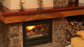 A stone fireplace with a fire, a wooden mantel, and a stack of firewood.