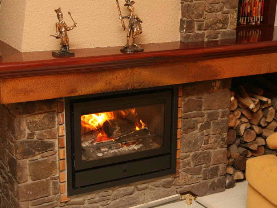 A stone fireplace with a fire, a wooden mantel, and a stack of firewood.