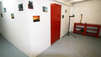 A hallway with a red door, a red bench, and several small pictures on the wall.