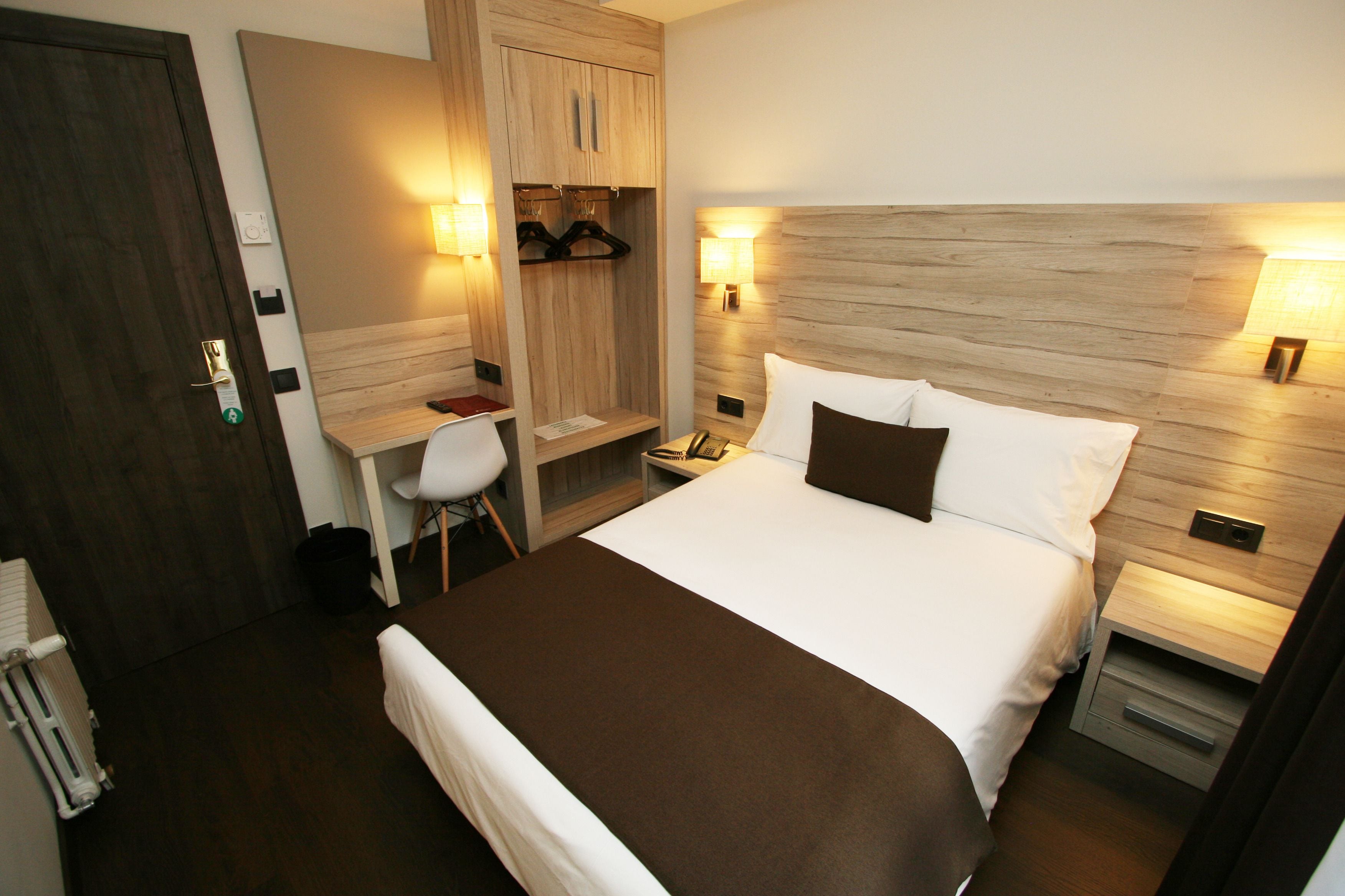 A hotel room with a large bed, a desk with a chair, a wardrobe, and two bedside lamps.