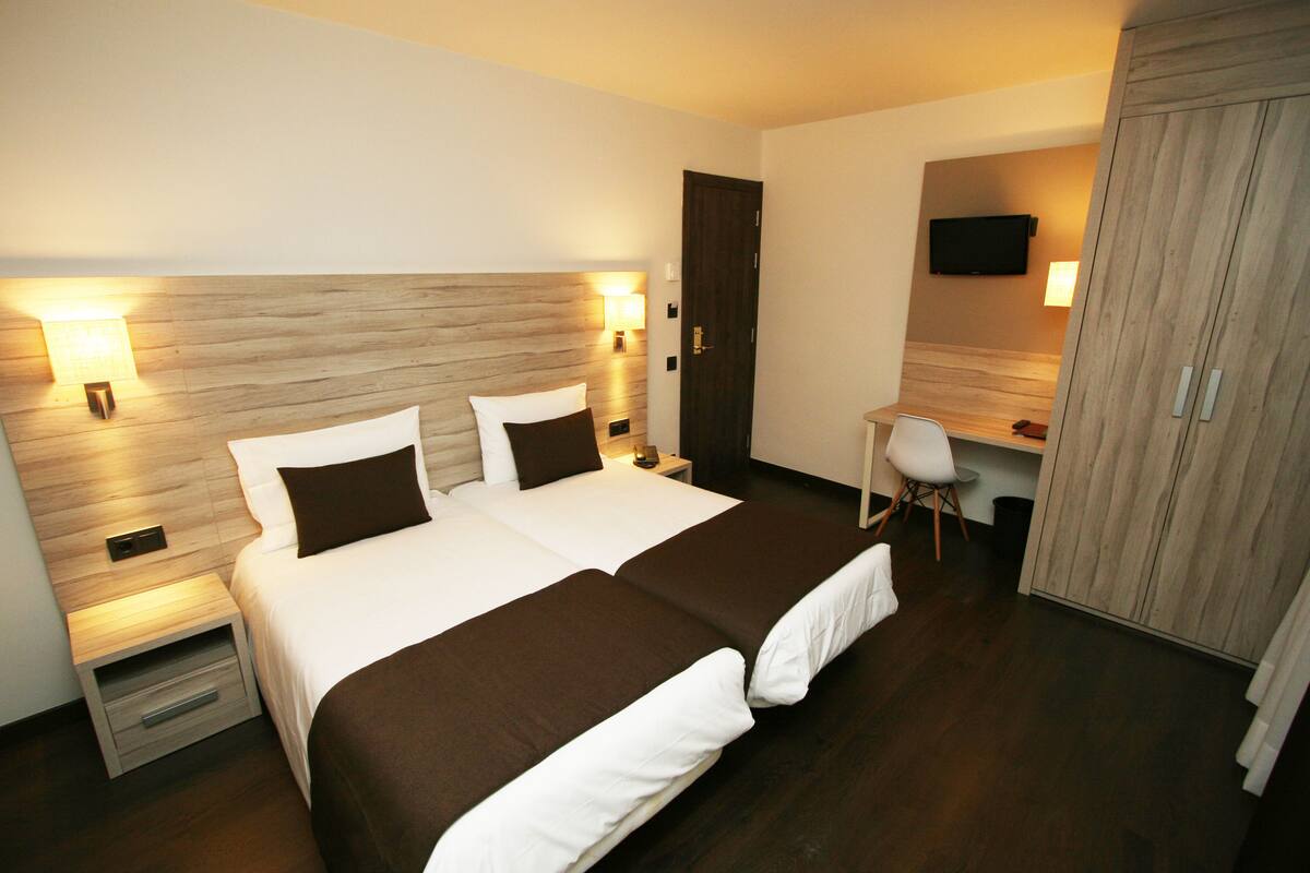 Ein Hotelzimmer mit Doppelbett, Nachttischen, einem Schreibtisch und einem Fernseher.