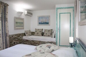 Ein Schlafzimmer mit zwei Betten, einer Wand aus Stein, einem Segelbootbild und einer türkisblauen Tür.