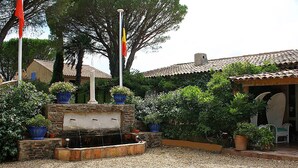 A traditional building with a tiled roof, a fountain, and potted plants. - Athénopolis (Grimaud)