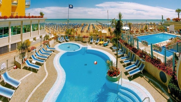 A resort pool area with multiple sun loungers and a central swimming pool. - Capri (Jesolo)