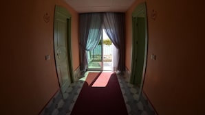 A hallway with a red carpet leading to a glass door, green doors on either side, and a ceiling with recessed lighting. - Capri (Jesolo)