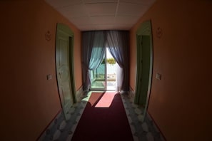 A hallway with a red carpet leading to a glass door, green doors on either side, and a ceiling with recessed lighting. - Capri (Jesolo)