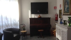 A living room with a television, piano, and a fireplace. - Capri (Jesolo)