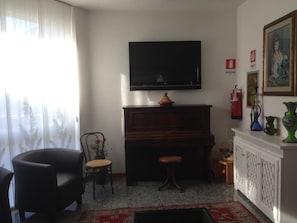 A living room with a television, piano, and a fireplace. - Capri (Jesolo)