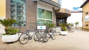 A hotel entrance with a bike rack, potted plants, and a sign for Hotel Capri. - Capri (Jesolo)