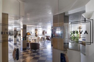 A modern interior of The Riva Beach Cafe with a checkered floor, contemporary furniture, and glass partitions.