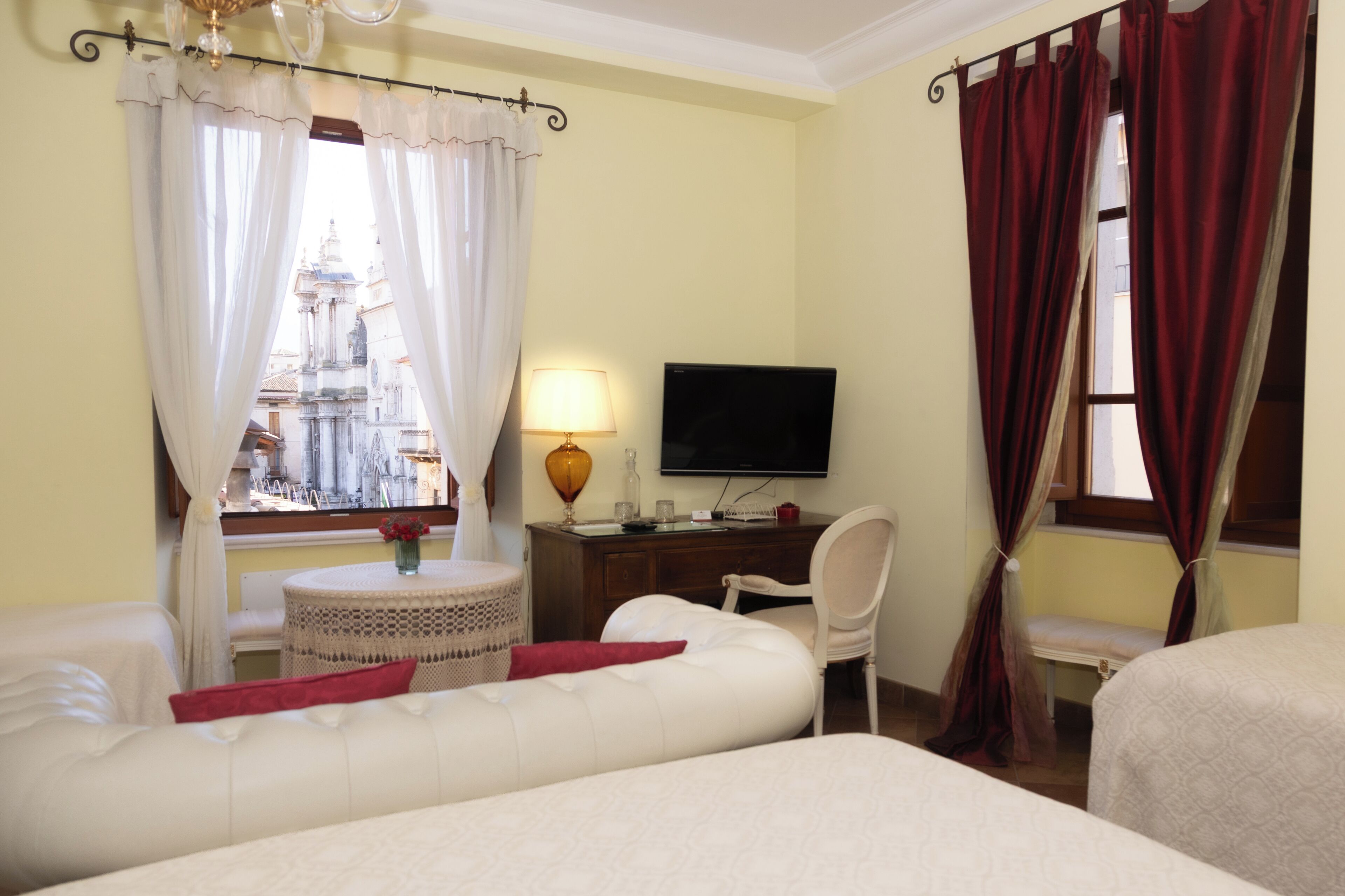 Quarto de hotel com cama, escrivaninha com televisão, uma cadeira e vista para um edifício pela janela.