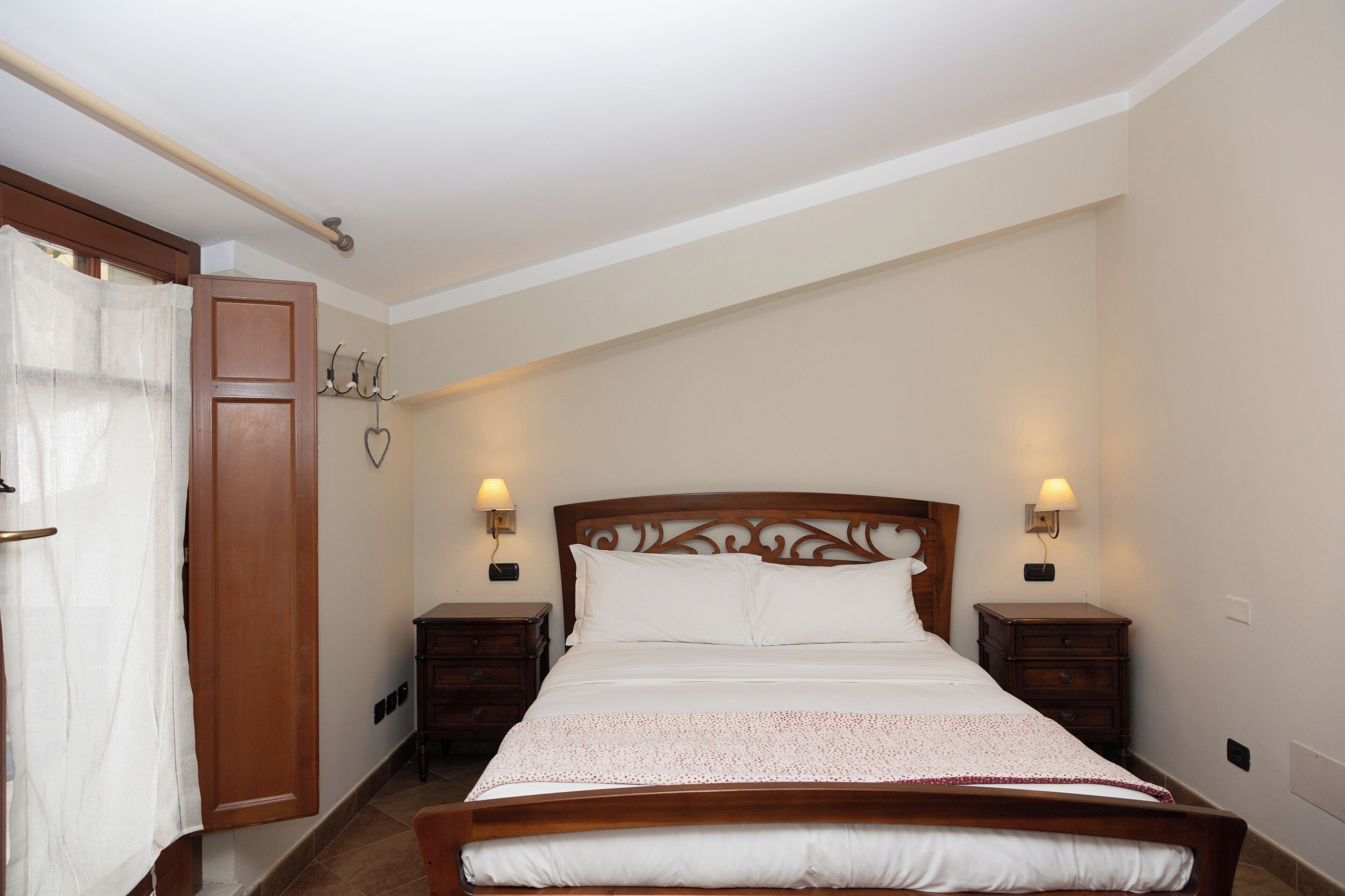 Ein Schlafzimmer mit einem hölzernen Bett, zwei Nachttischen mit Lampen, einem Holzschrank und einem Vorhang.