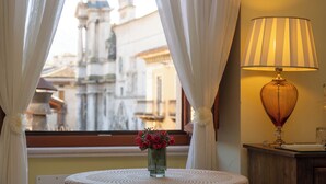 Una habitación con vista a un edificio histórico, un florero con flores sobre una mesa y una lámpara en una mesita de noche.