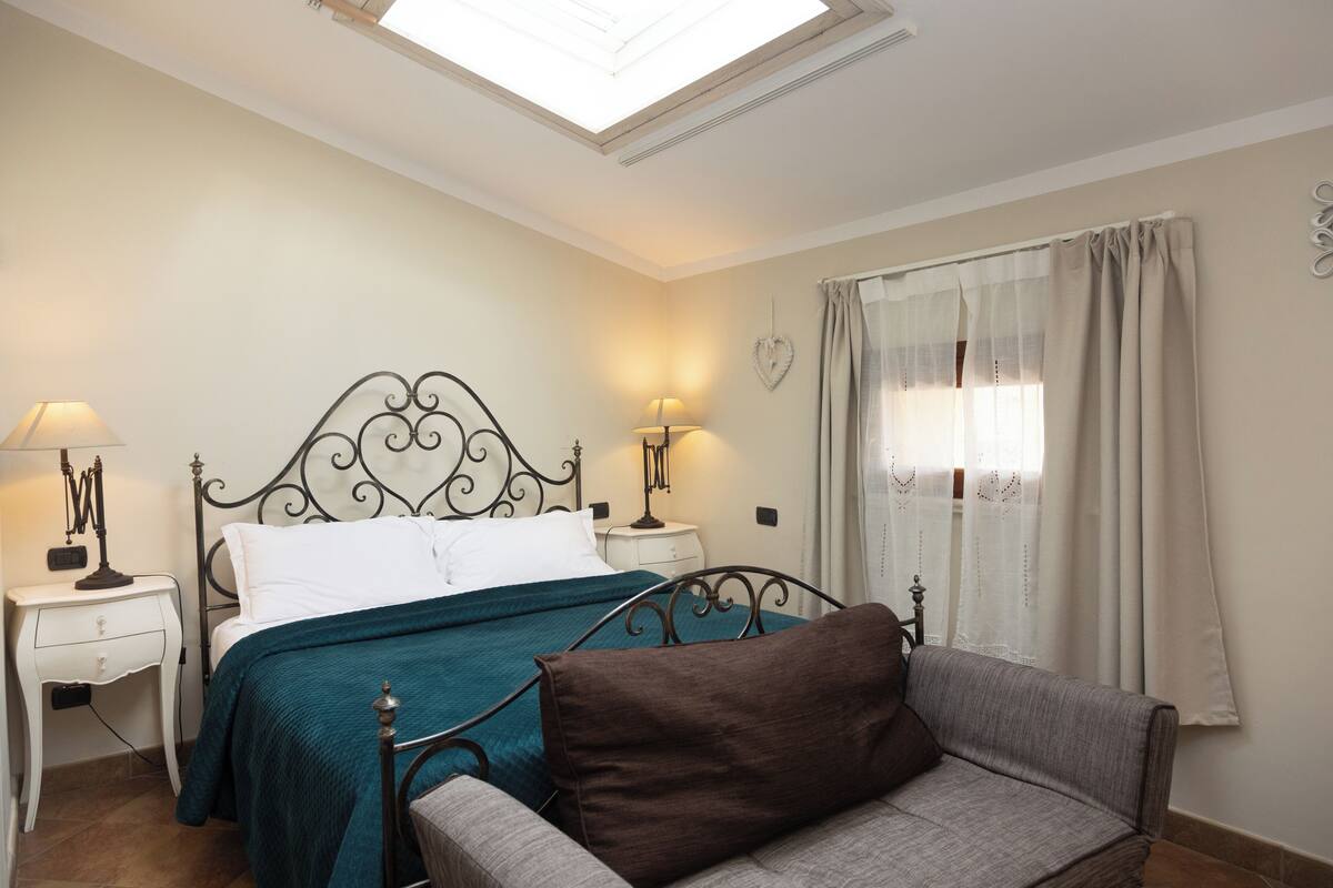 Un dormitorio con una cama, dos mesitas de noche, un sofá y una ventana con cortinas.