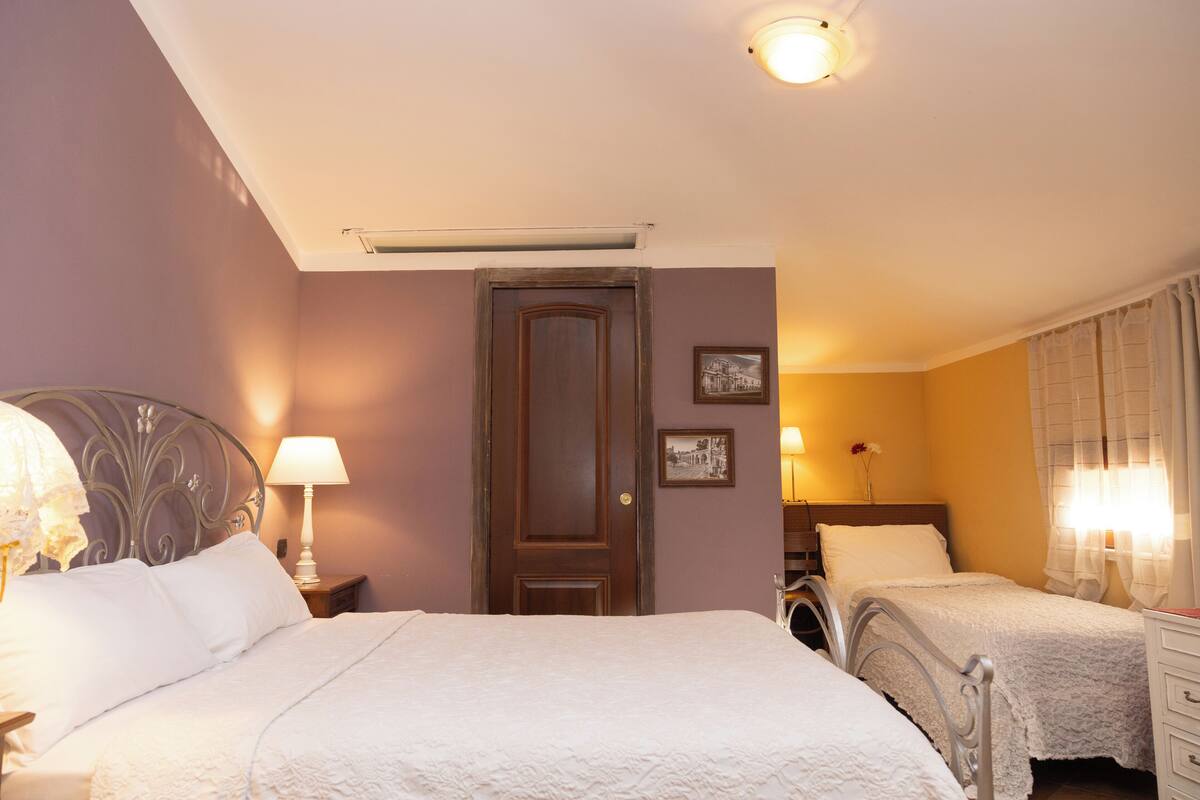 Habitación de hotel con dos camas, una puerta de madera, una mesita de noche con lámpara y un cuadro colgado en la pared.