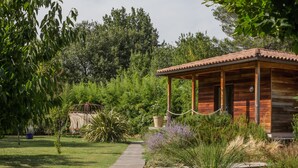 A wooden cabin with a tiled roof, surrounded by lush greenery and a wooden deck. - Le Verger Maelvi (Grimaud)