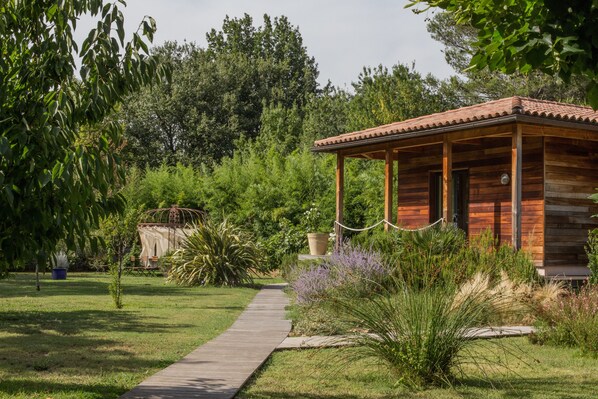 A wooden cabin with a tiled roof, surrounded by lush greenery and a wooden deck. - Le Verger Maelvi (Grimaud)