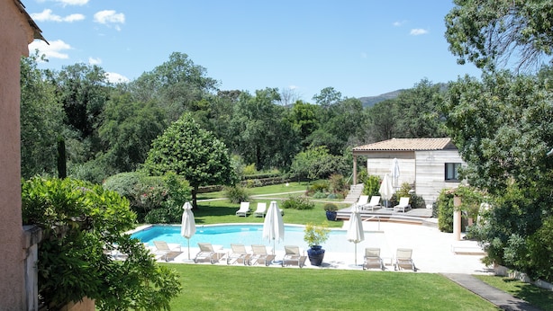 A pool area with lounge chairs and umbrellas, surrounded by lush greenery and a mountain backdrop. - Le Verger Maelvi (Grimaud)