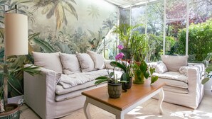 A conservatory with a white sofa, a wooden table, and various potted plants. - Le Verger Maelvi (Grimaud)