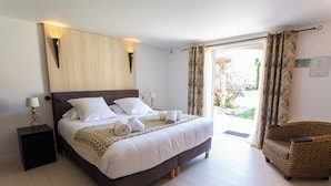 A neatly made bed with white linens and rolled towels, a dark wooden headboard, a small bedside table with a lamp, and a wicker armchair. - Le Verger Maelvi (Grimaud)