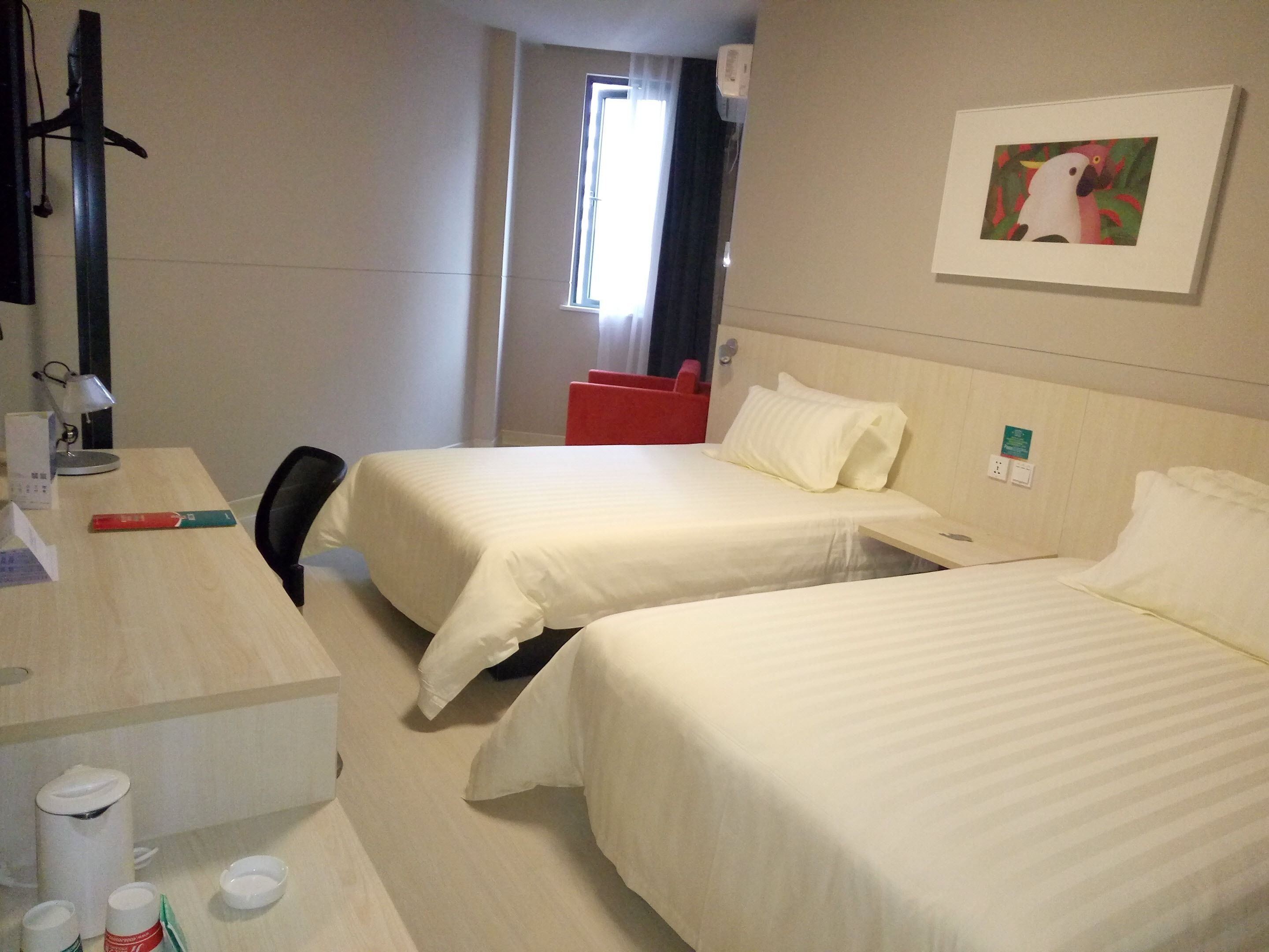 Ein Hotelzimmer mit zwei Betten, einem Schreibtisch mit Lampe, einem Sessel und einem Fenster mit Vorhängen.