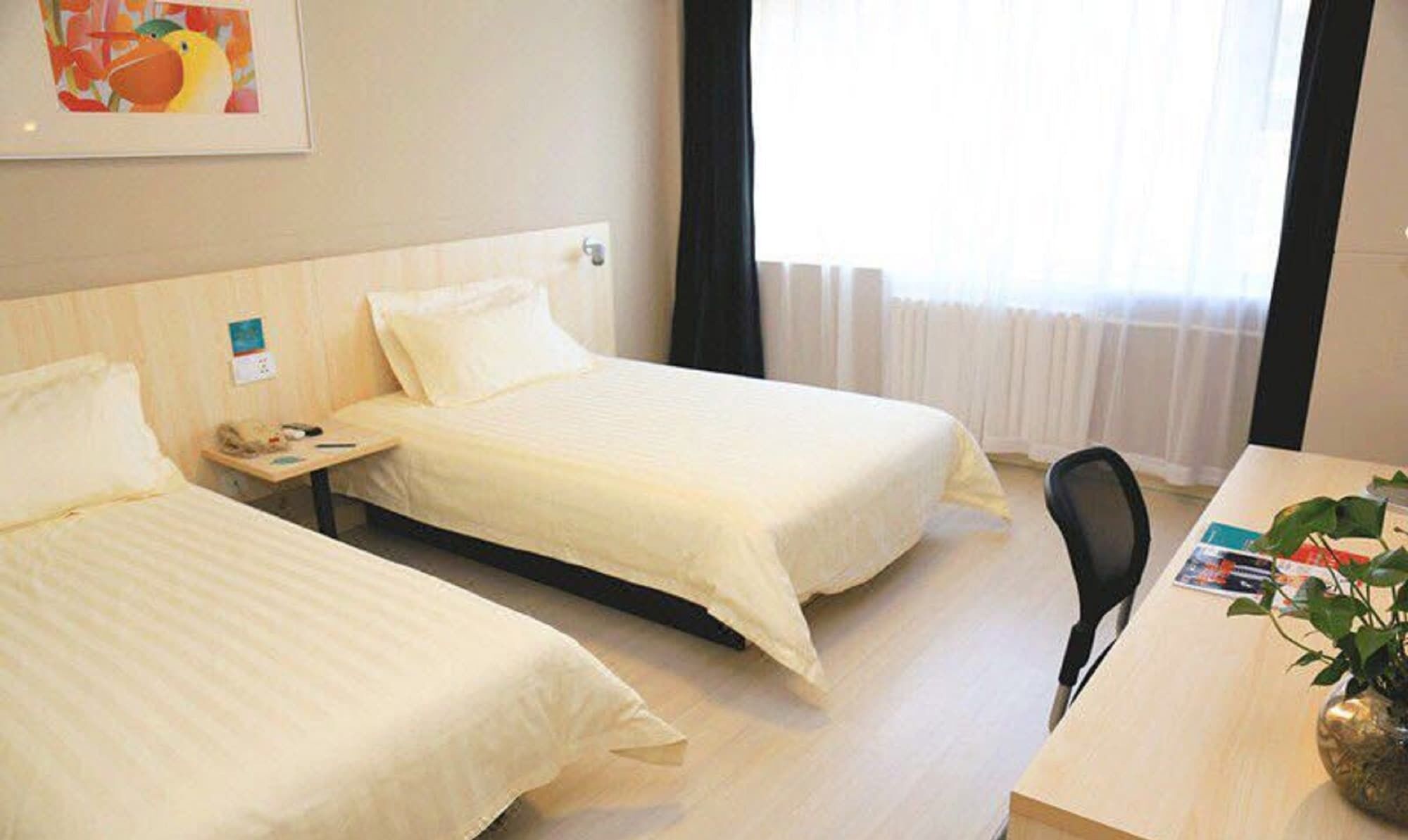 A hotel room with two beds, a desk, a chair, and a window with curtains.