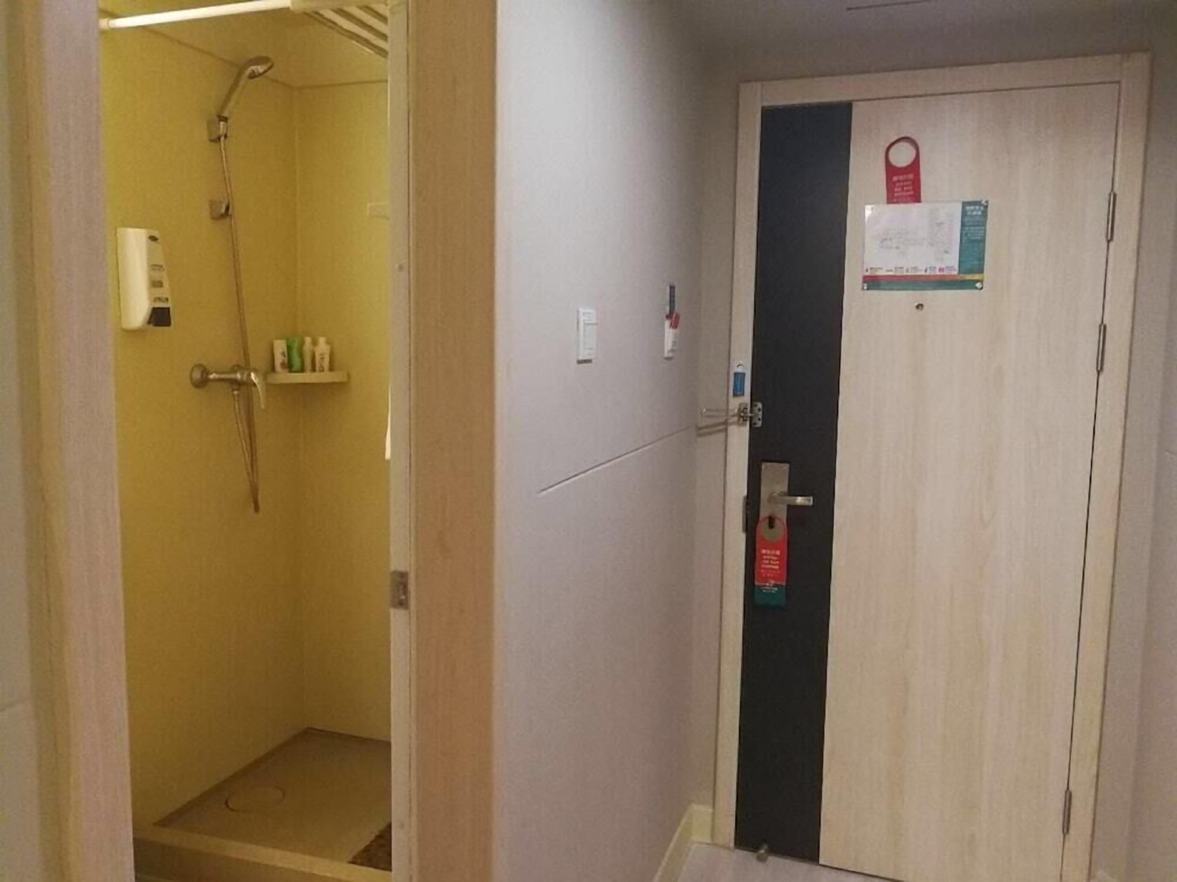 Ett hotellrum med dusch, en dörr med lås och en liten hylla med toalettartiklar.