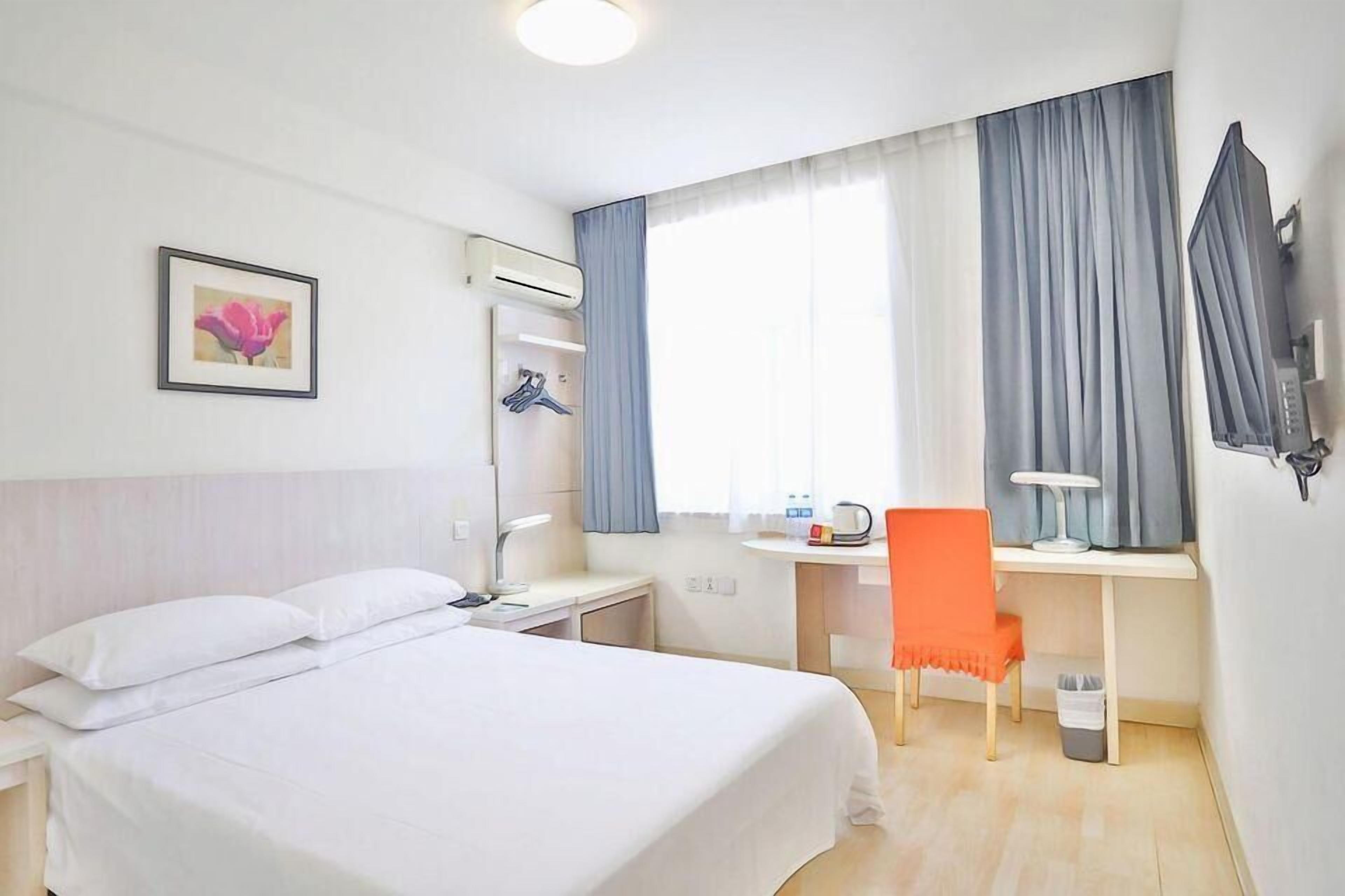 A hotel room with a bed, desk, chair, and a picture on the wall.