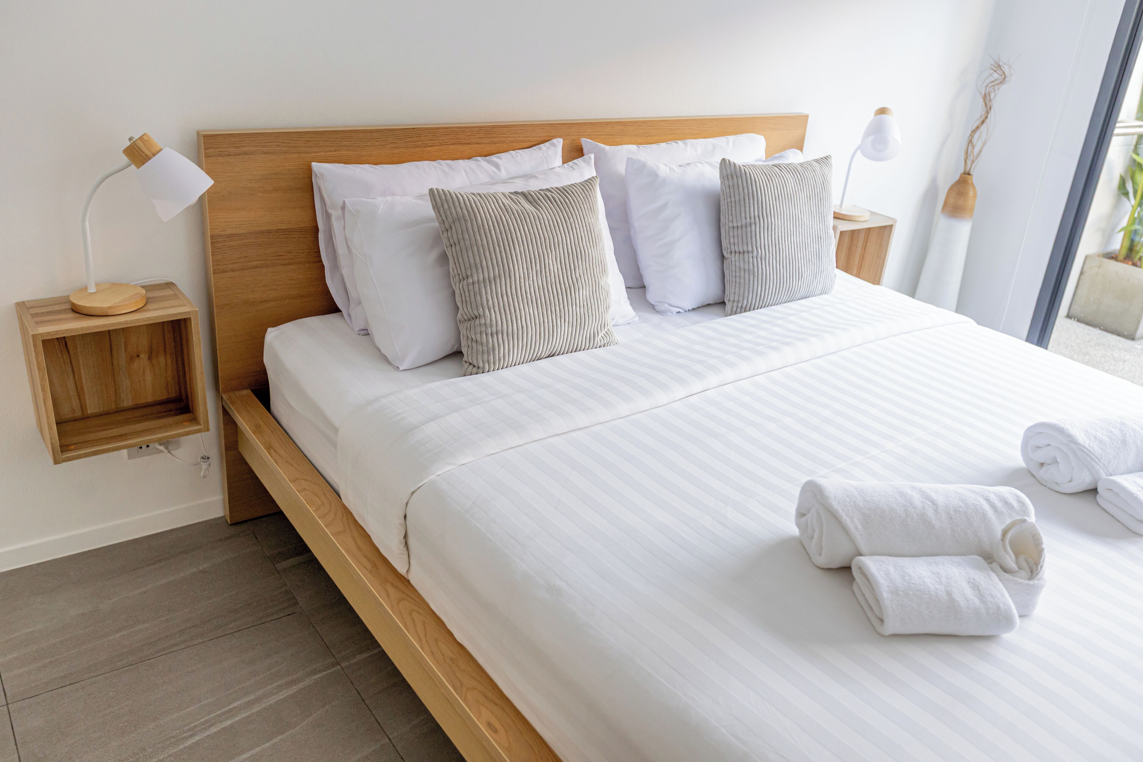 A neatly made bed with white linens and striped pillows, a wooden headboard, and two bedside tables with lamps.