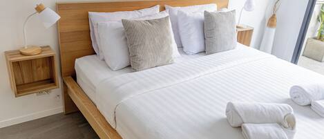 A neatly made bed with white linens and striped pillows, a wooden headboard, and two bedside tables with lamps.