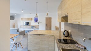 A modern kitchen with granite countertops, wooden cabinets, and stainless steel appliances. There is a dining area with a table and chairs, and a living room with a sofa and a TV. - Studio365 Apartment (Chiang Mai)