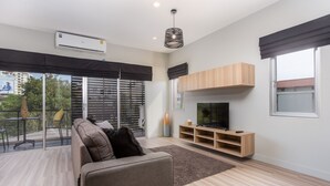 A modern living room with a sofa, TV, and wooden shelves. - Studio365 Apartment (Chiang Mai)