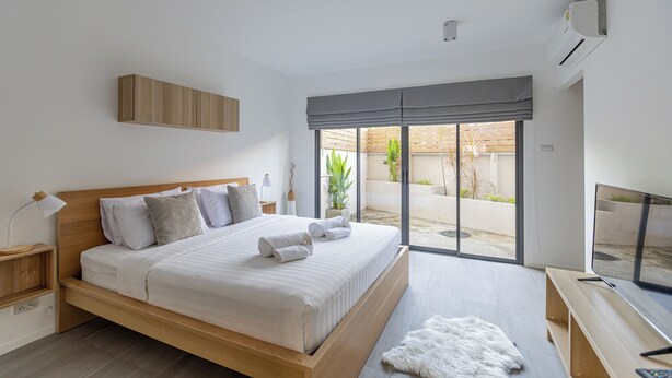 A modern bedroom with a large bed, a TV, and a sliding glass door to an outdoor area. - Studio365 Apartment (Chiang Mai)
