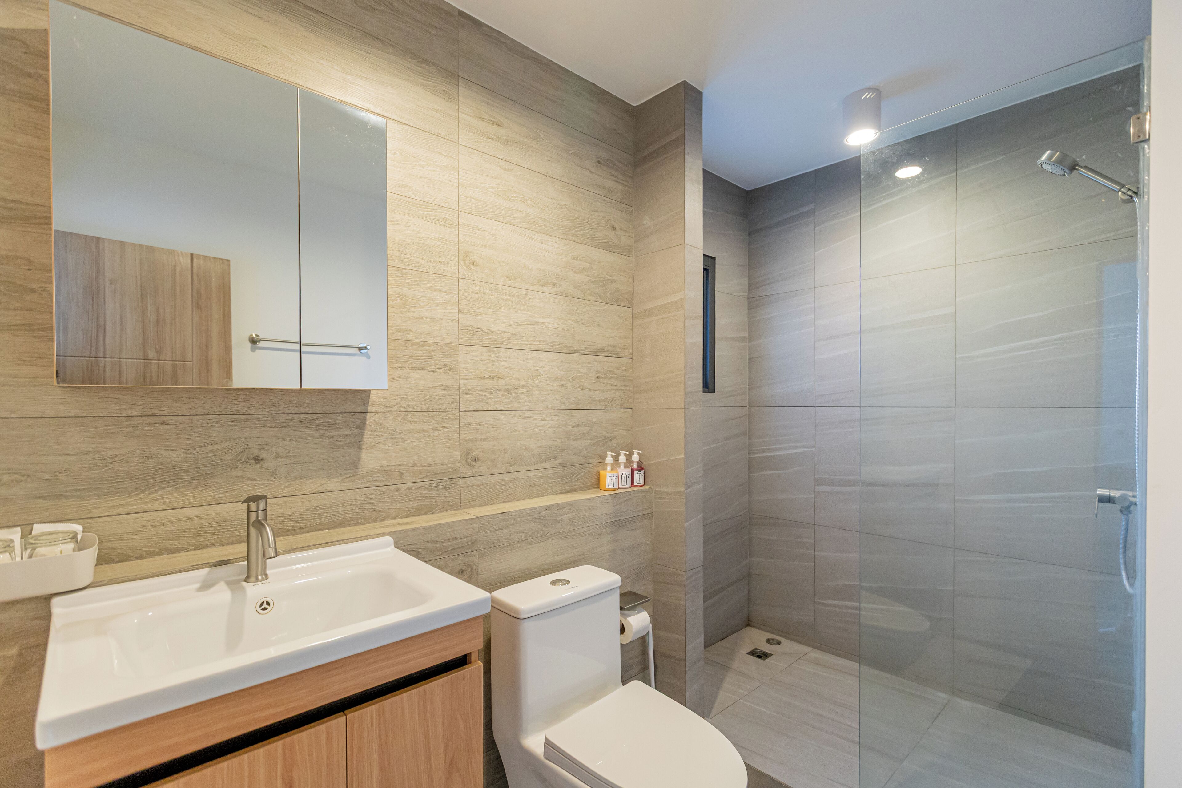 A modern bathroom with a wooden vanity, a large mirror, a shower enclosure, and a toilet.
