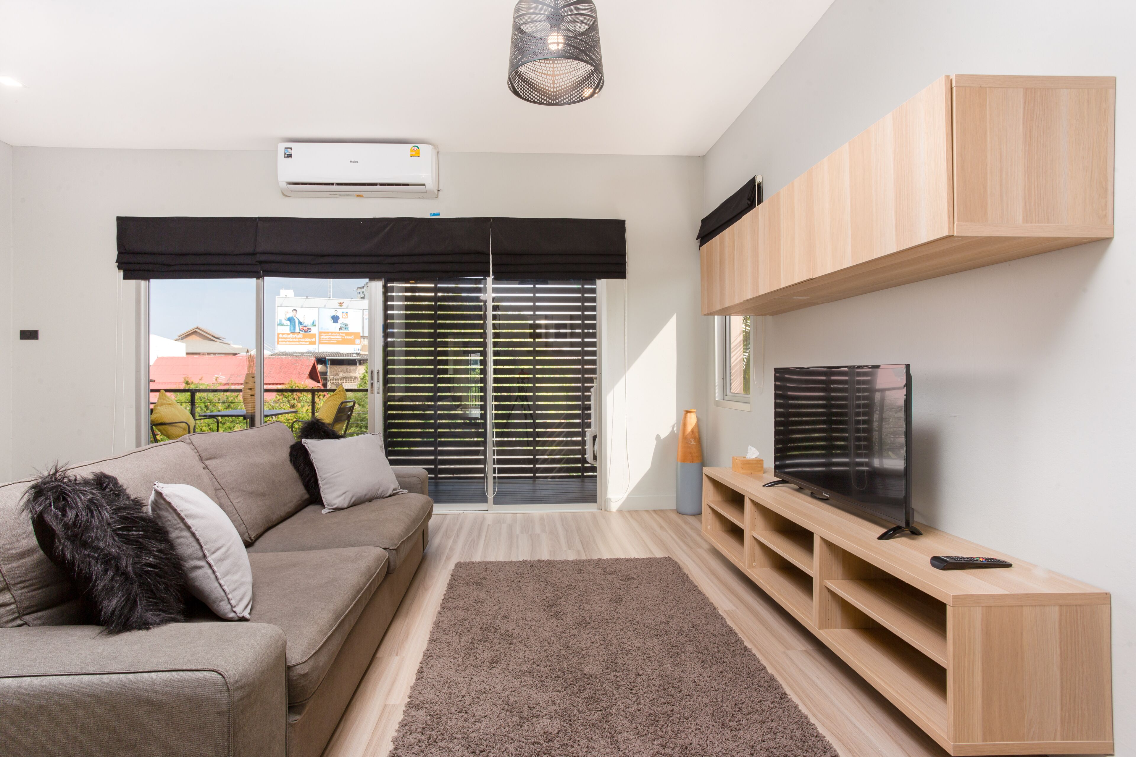 A modern living room with a sofa, a TV on a wooden stand, and a large window with blinds.
