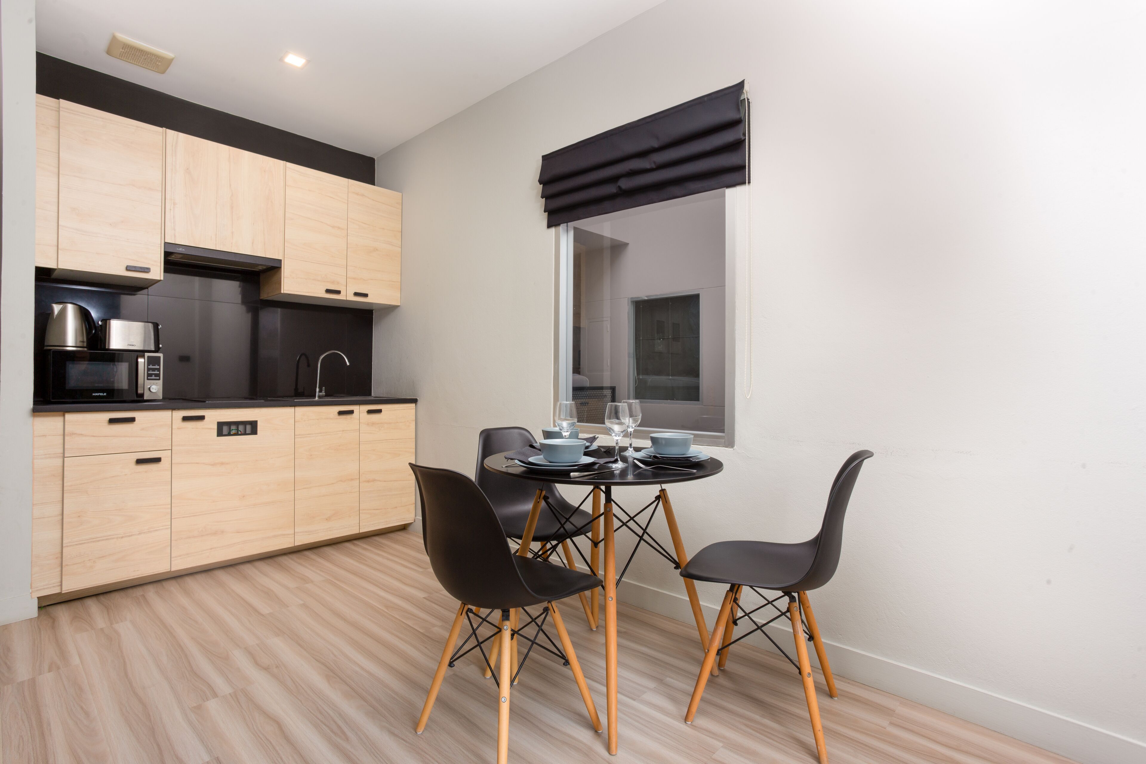 Una cocina moderna con armarios de madera, encimera negra y comedor con una mesa redonda y cuatro sillas.