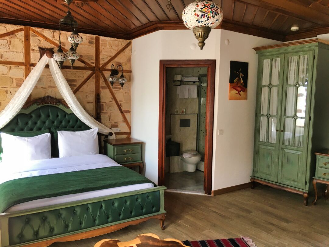 A room with a green bed, wooden ceiling beams, a green cabinet, and a door leading to a bathroom.