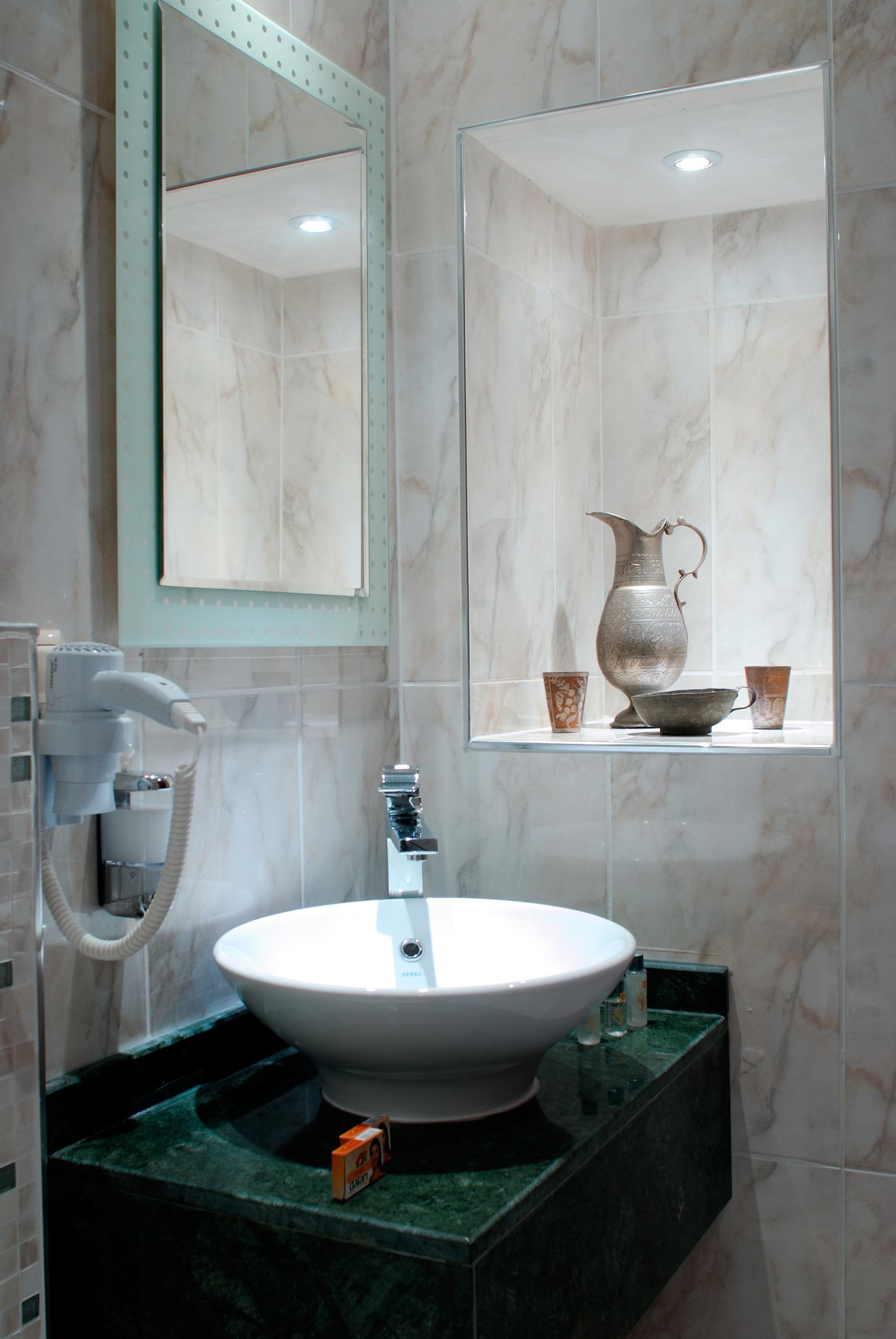 Une salle de bain avec un lavabo blanc, un miroir et une étagère sur laquelle se trouvent un pichet et des tasses.