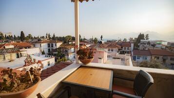 Un balcón con mesa y sillas, con vista a una zona residencial con casas y una montaña al fondo.