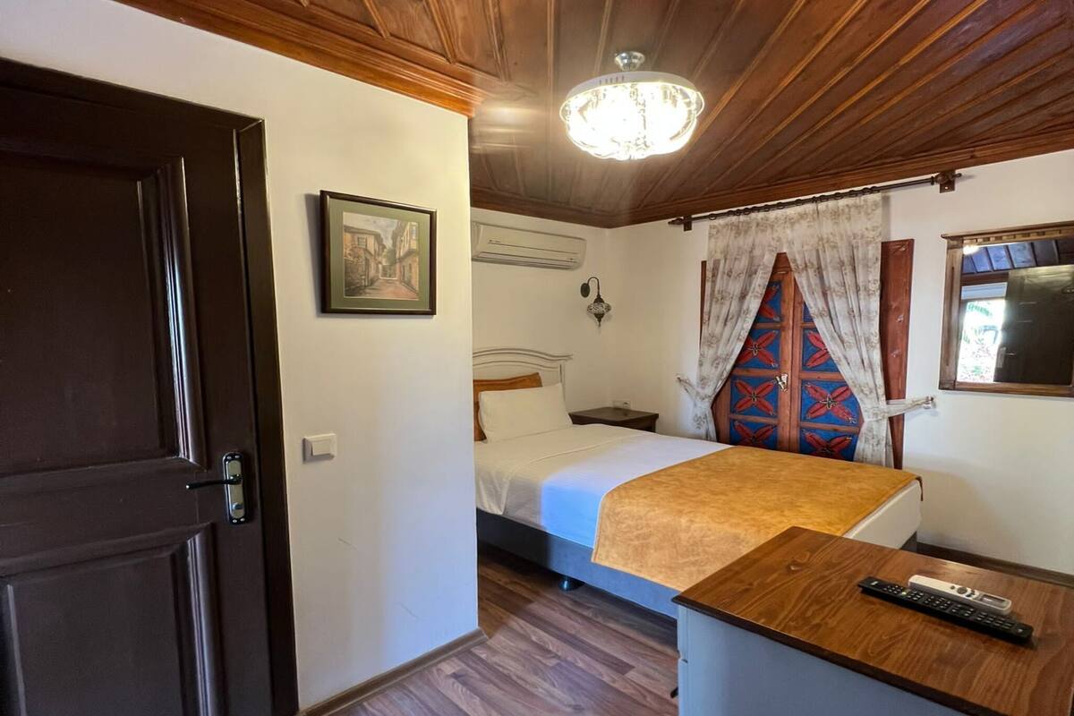 A room with a wooden ceiling, a bed with a blue headboard, a bedside table with a remote control, and a door with a handle.