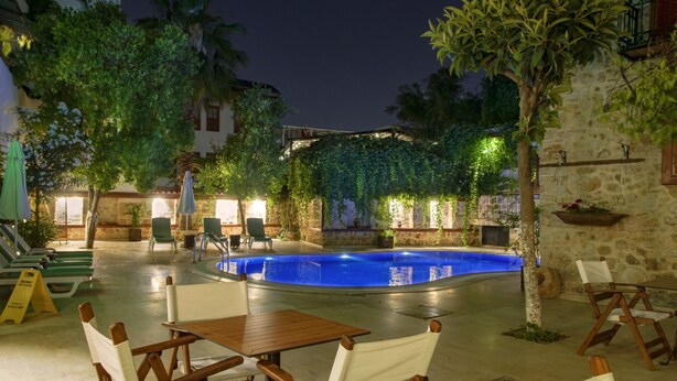 A pool area with lounge chairs and tables, surrounded by greenery and stone walls.