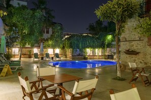 Un área de piscina con sillas reclinables y mesas, rodeada de vegetación y muros de piedra.