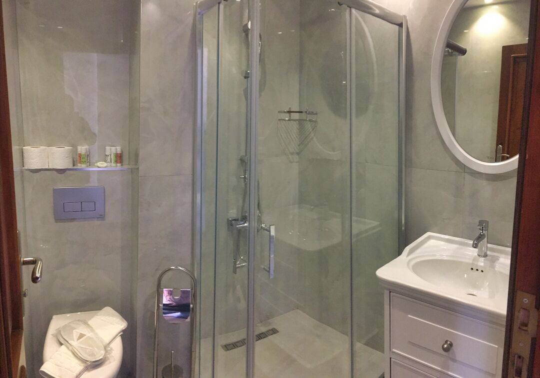 Un baño moderno con ducha de vidrio, un lavabo blanco con espejo y un inodoro con toalla.