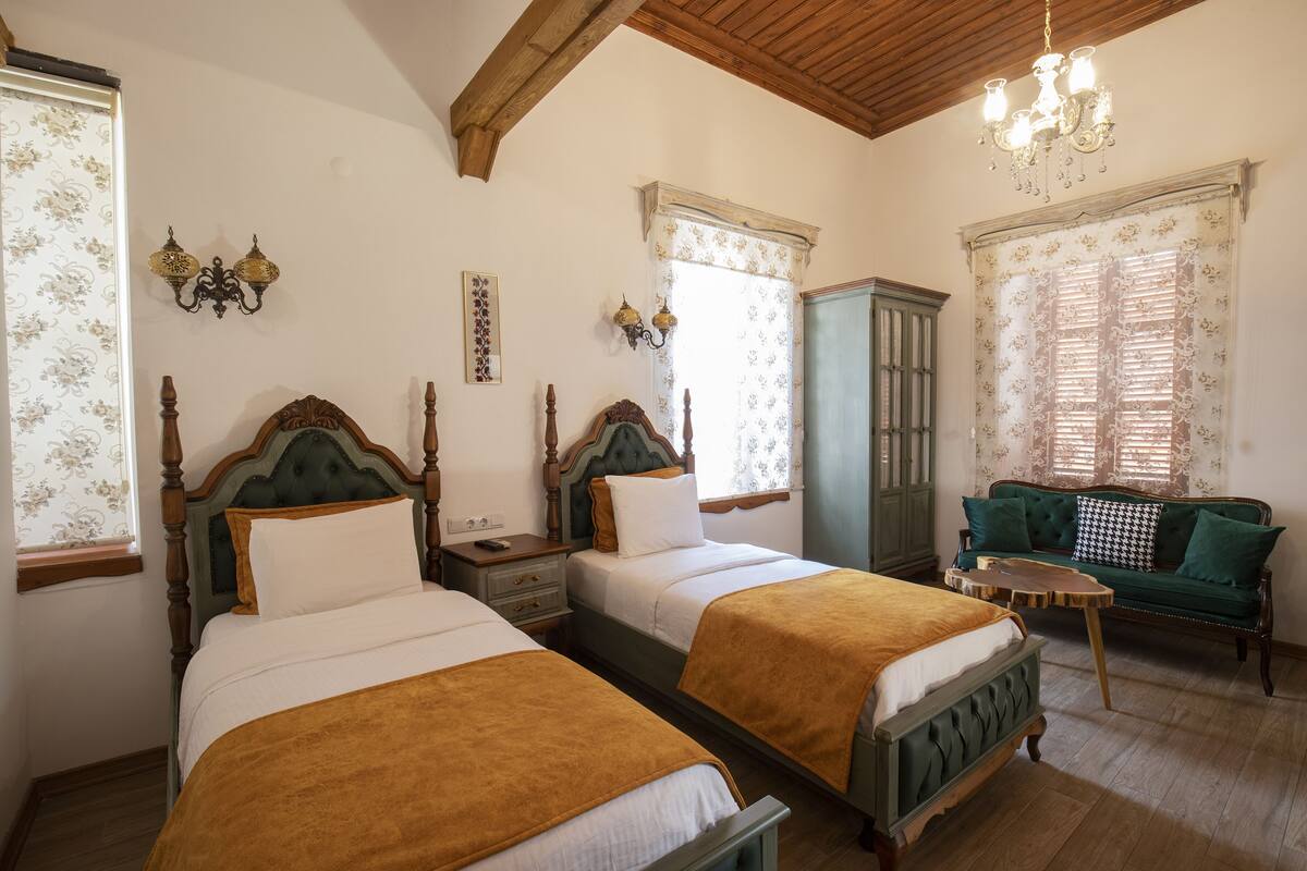 A room with two wooden beds, a green sofa, a small wooden table, and a chandelier.