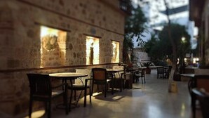 An outdoor cafe with stone walls and tables, featuring a view of the cityscape in the background.