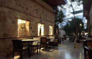 An outdoor cafe with stone walls and tables, featuring a view of the cityscape in the background.