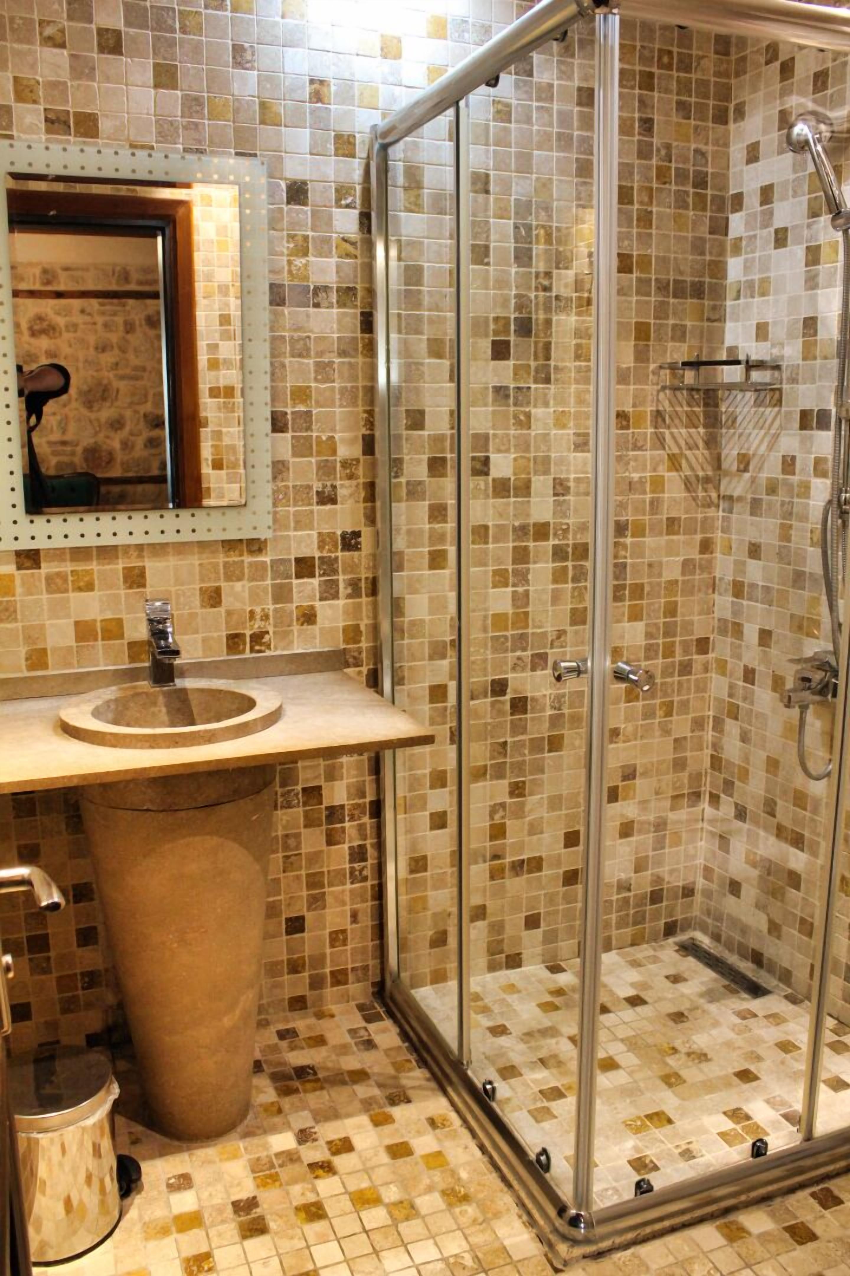 Un baño con ducha separada por mampara de vidrio, lavamanos con espejo y suelo de baldosas.