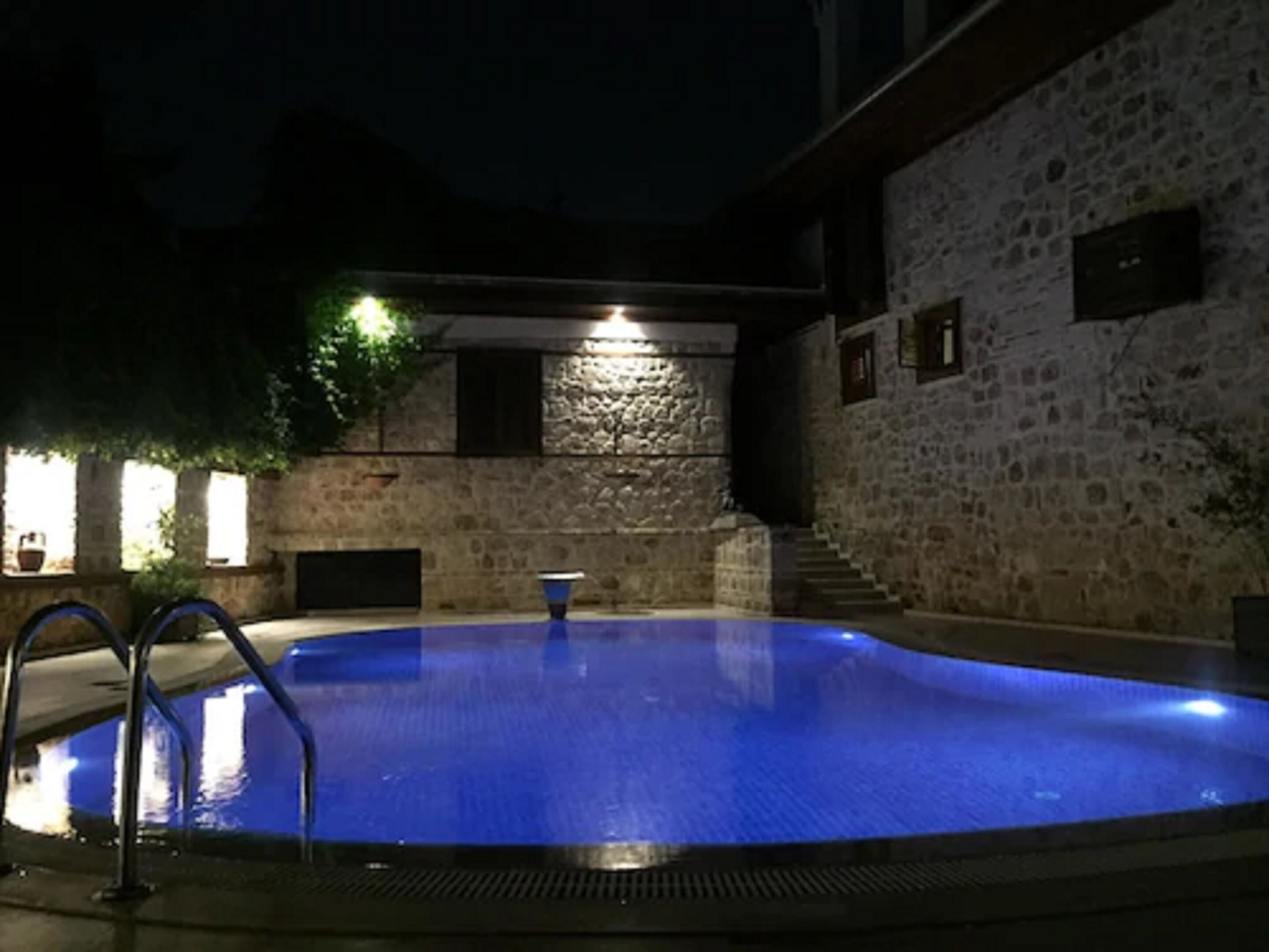 A swimming pool with a stone wall and a staircase leading up to a lit area.