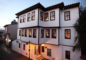 A multi-story building with white walls and dark trim, featuring multiple windows and a staircase leading to the entrance.