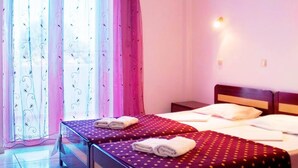 A hotel room with two beds, a large window with curtains, and a nightstand with a lamp.